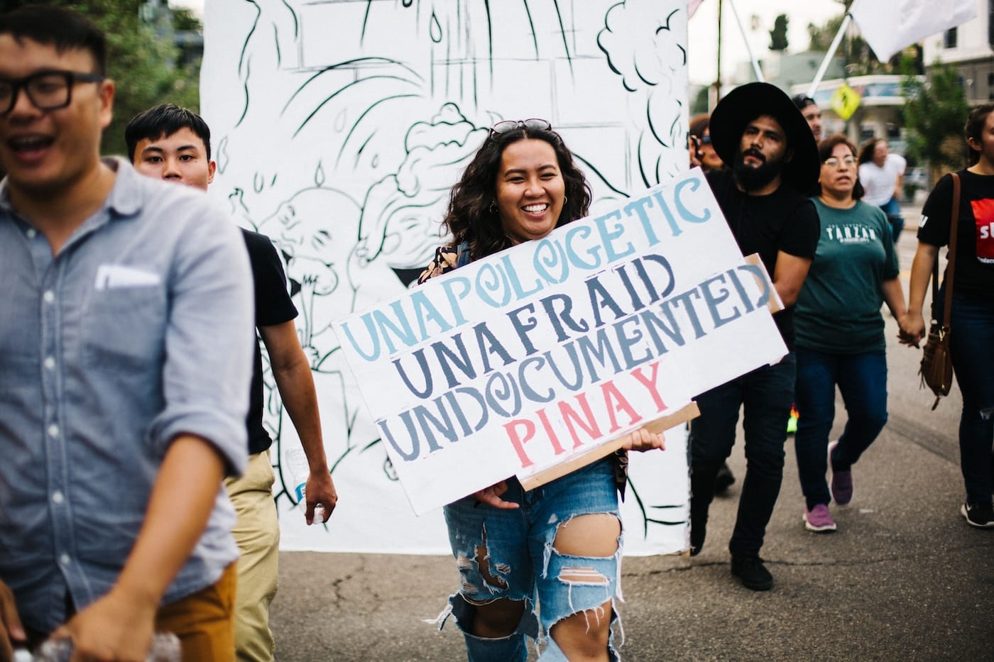 A woman with brown hair and ripped jeans holds a sign during a immigrants rights march in Los Angeles