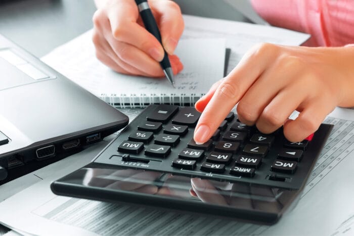 Female in the office uses a calculator and writes data in a notebook to calculate USCIS biometrics fees