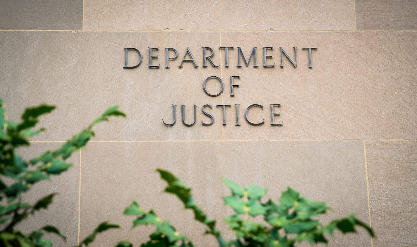 Stone EOIR building with words "Department of Justice" written on the facade with green plants in the foreground