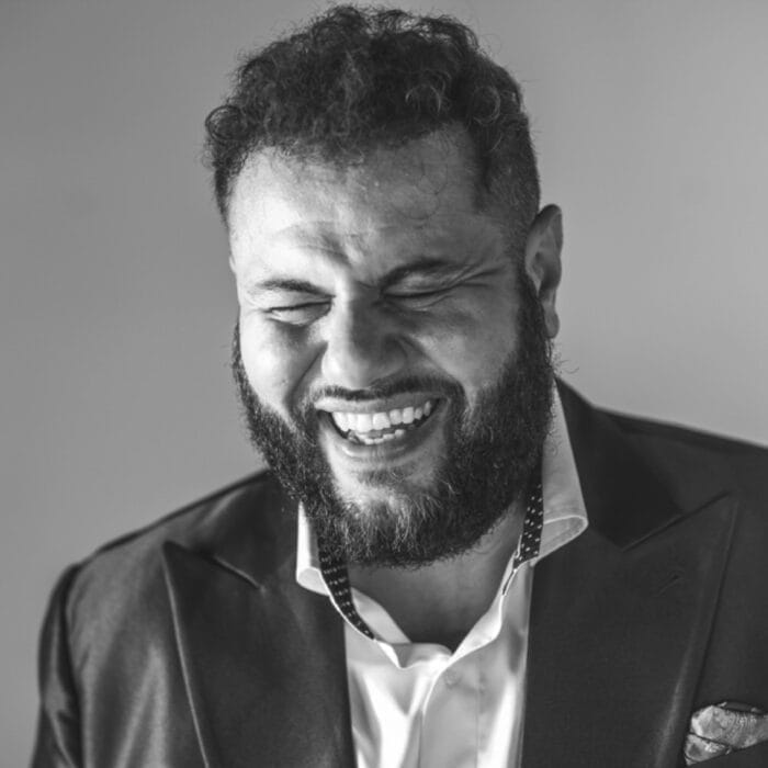 black and white photo of a man with a beard wearing a suit jacket and white button-up shirt laughing and closing his eyes