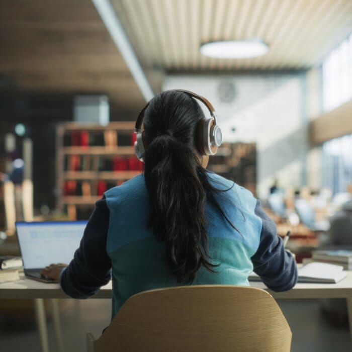 Female student on laptop in a public library working on university homework, staying informed to avoid F-1 visa OPT scams.