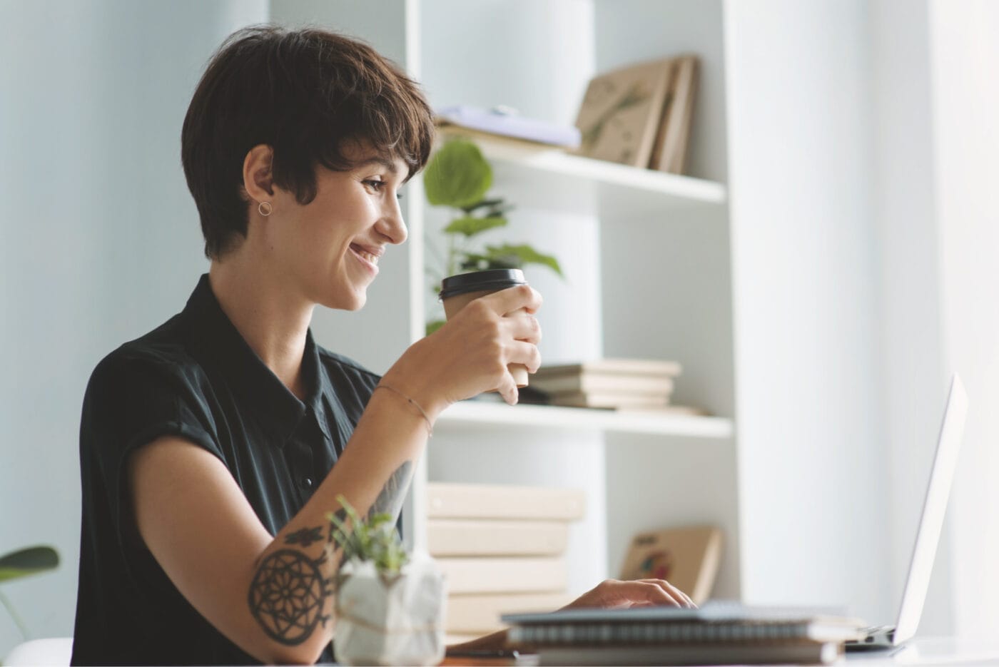 Photo of young businesswoman working on laptop and smiling while sitting at her desk